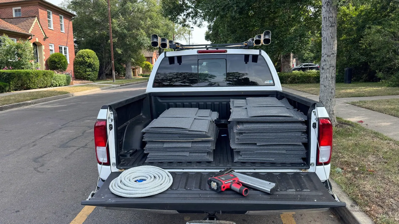 A roofing truck loaded with shingle bundles, rope, a nail gun and ladders, parked on a residential street in Clarksville, Tennessee